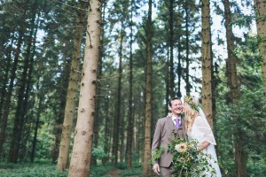 Bride kissing groom on cheek in woods