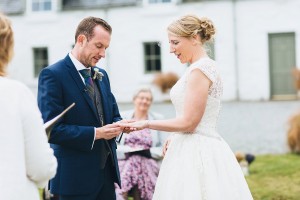 Groom placing ring on brides finger outdoor wedding ceremony