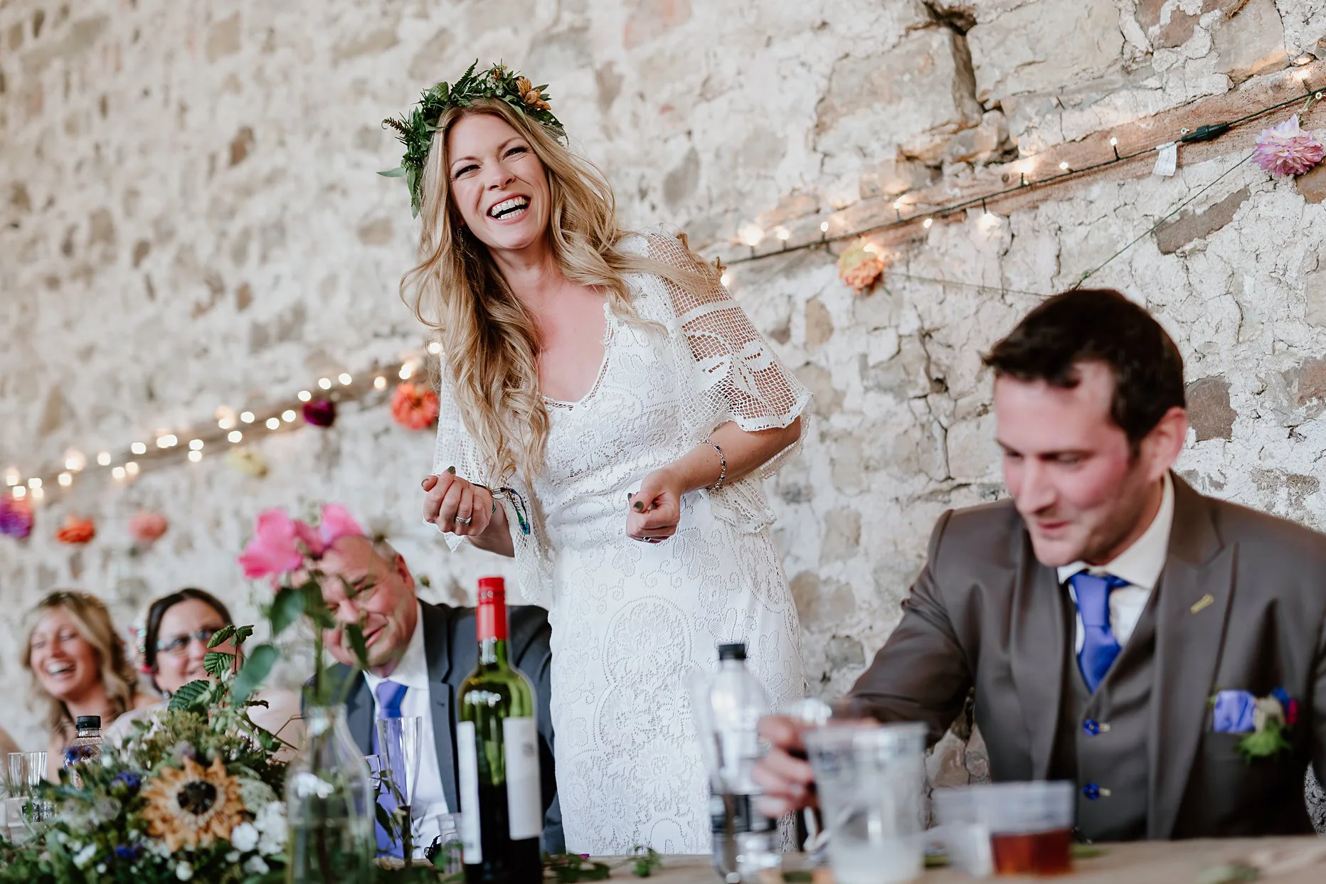 Bride giving her wedding speech at Camp Katur. Bride is smiling and laughing. She is wearing a white crochet wedding dress and flower crown.