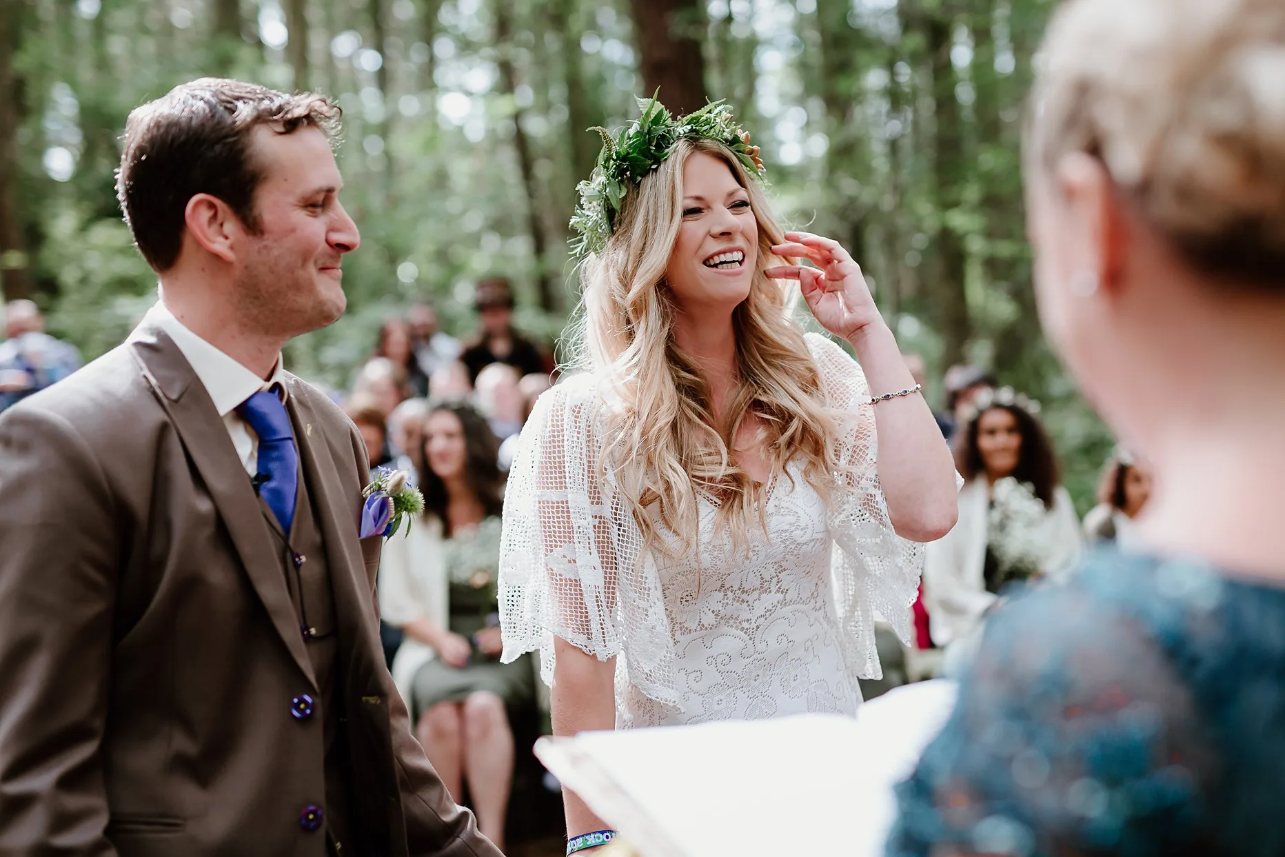 Bride laughing during woodland ceremony. Bride is wearing a white crochet wedding dress and green foliage flower crown. 