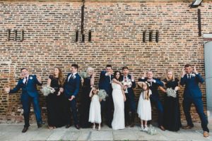 Bridal party laughing against brick wall