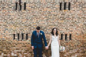 Bride and groom laughing against brick wall