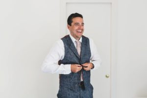 Groom buttoning up waistcoat for wedding