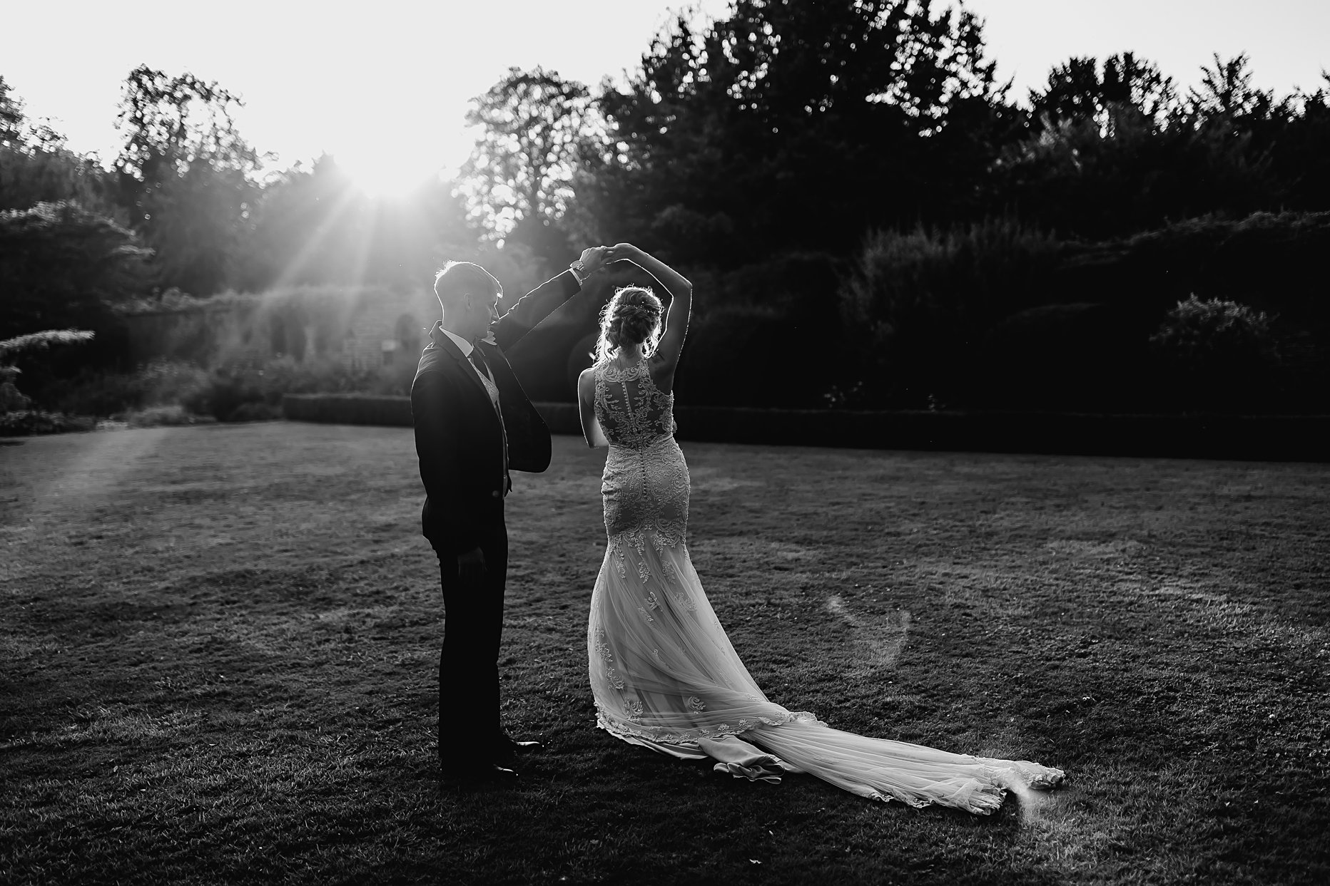 Black and white image of a bride and groom dancing in the sunset. The groom is spinning the bride around.
