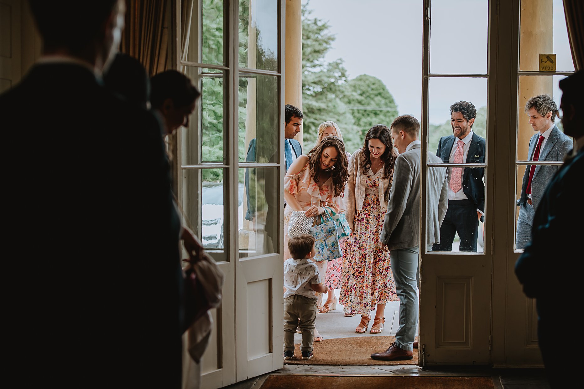 Guests arriving for a wedding at Saltmarshe Hall. The photo is taken from inside Saltmarshe hall and guests are framed by the door and windows.