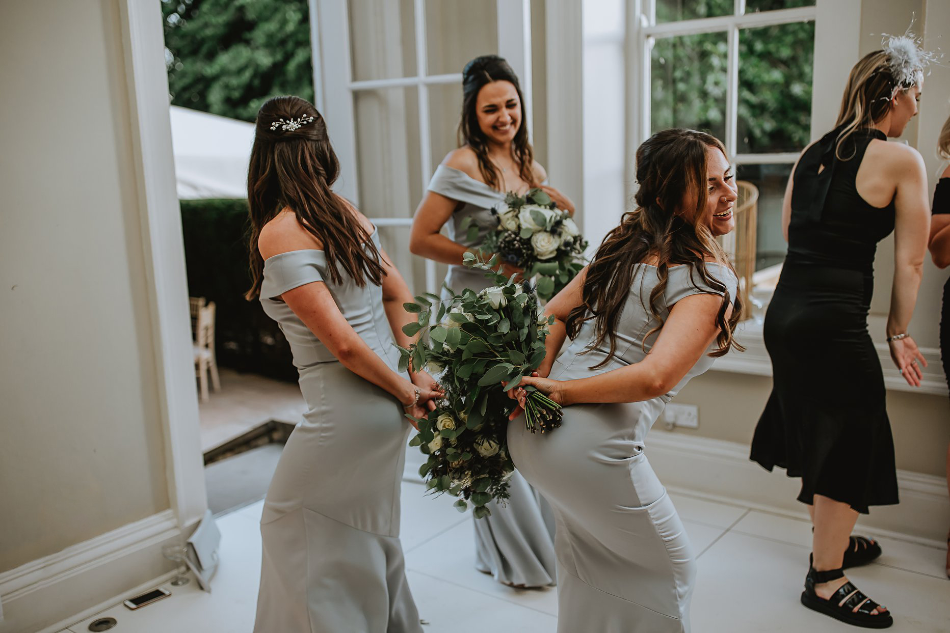 Two bridesmaids acting silly on the dance floor at Saltmarshe Hall. They are each holding a bouquet behind their back. 