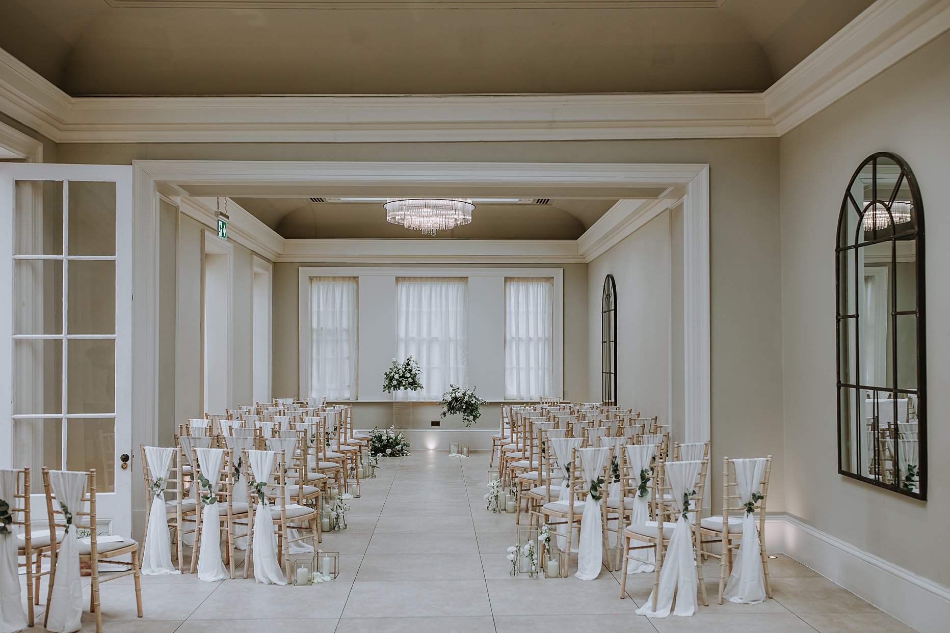 Interior photograph of the ceremony room at Saltmarshe Hall. The room is light and airy. Chairs and lined up down the room with white chair drapes and green foliage pined to the back. 