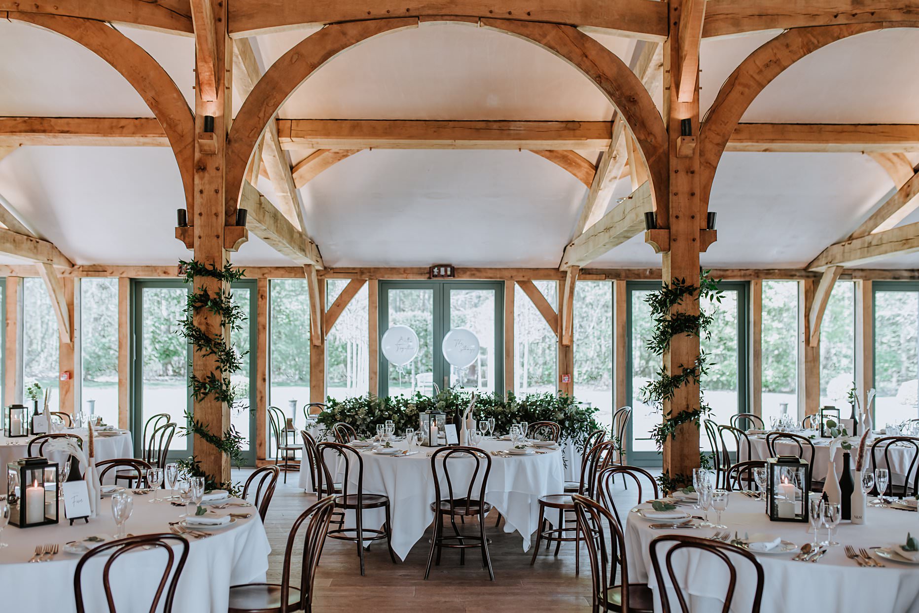 Interior of the wedding breakfast room at Hazel Gap Barn. The room is dressed with white table cloths and green foliage.