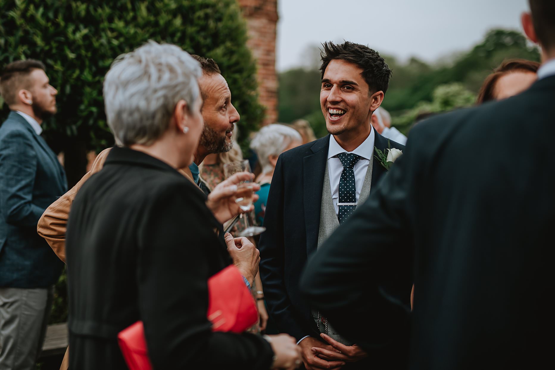 Groom chatting to his wedding guests during the drinks reception. He is happy and smiling.