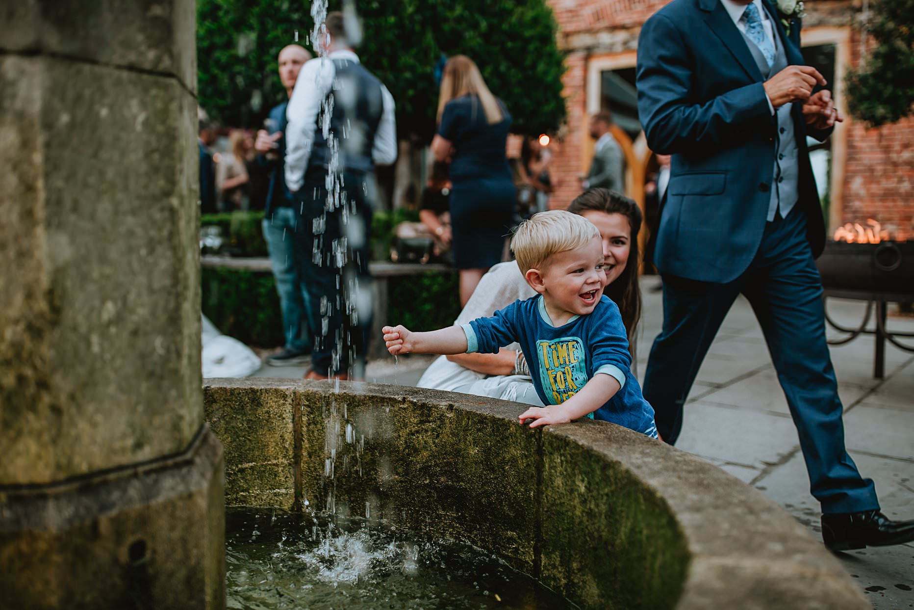 Young child playing with a water fountain in the courtyard of Hazel Gap Barn wedding venue.