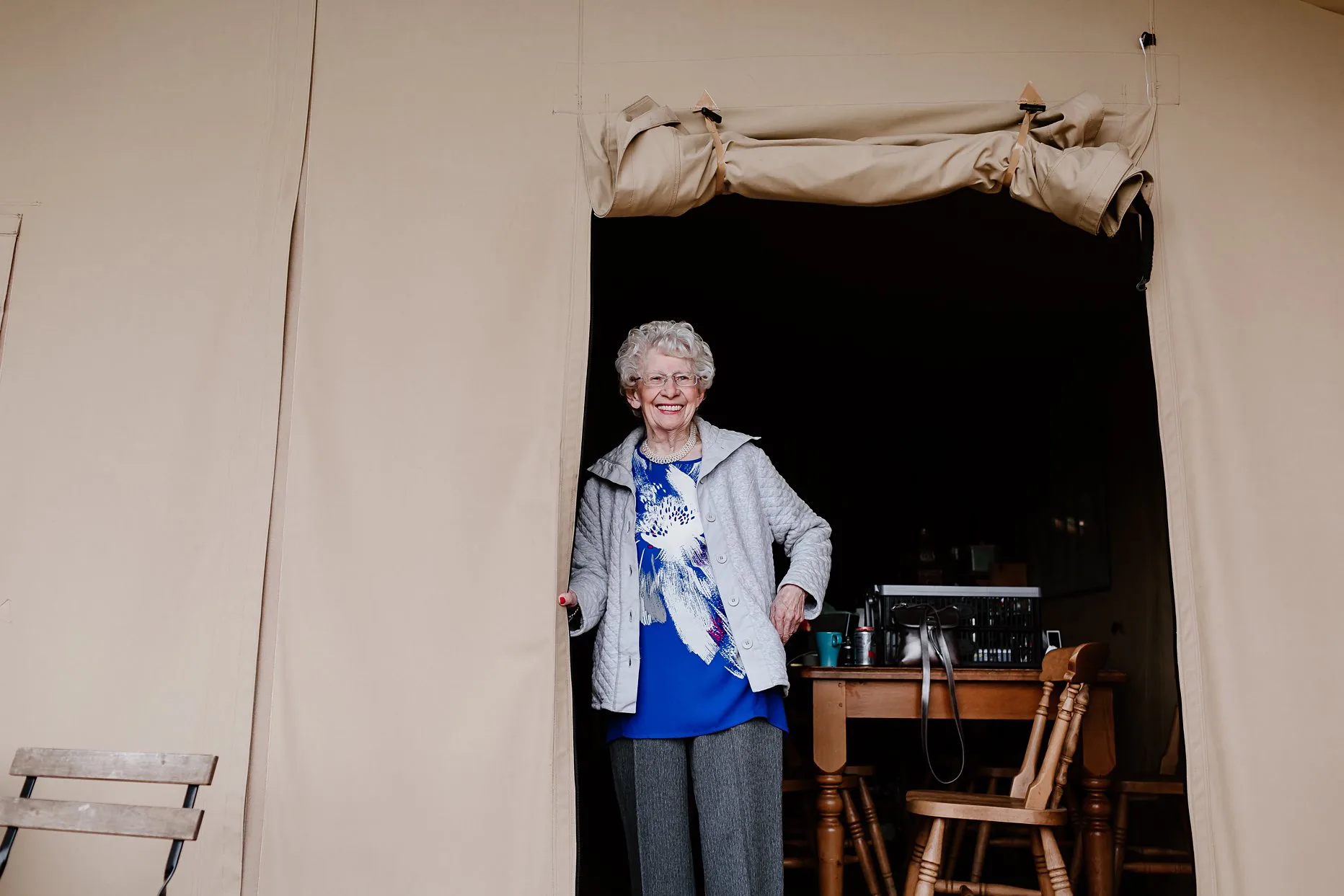 The brides grandma inside a glamping tent the morning of the wedding. She is smiling at the camera.