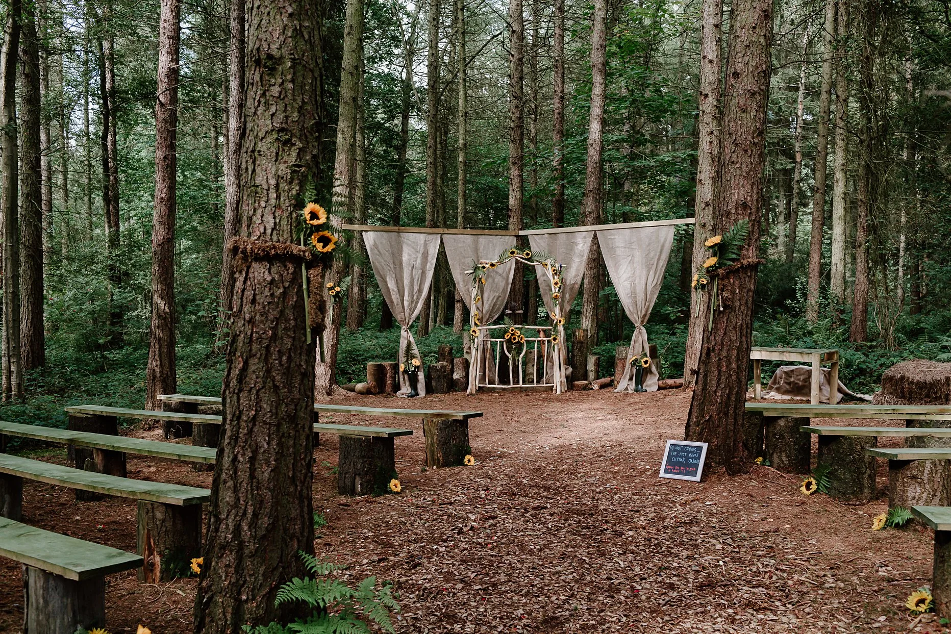 Ceremony space at Camp Katur. Outdoor wedding ceremony in the woods. The alter is decorated with yellow sunflowers and hessian drapes.