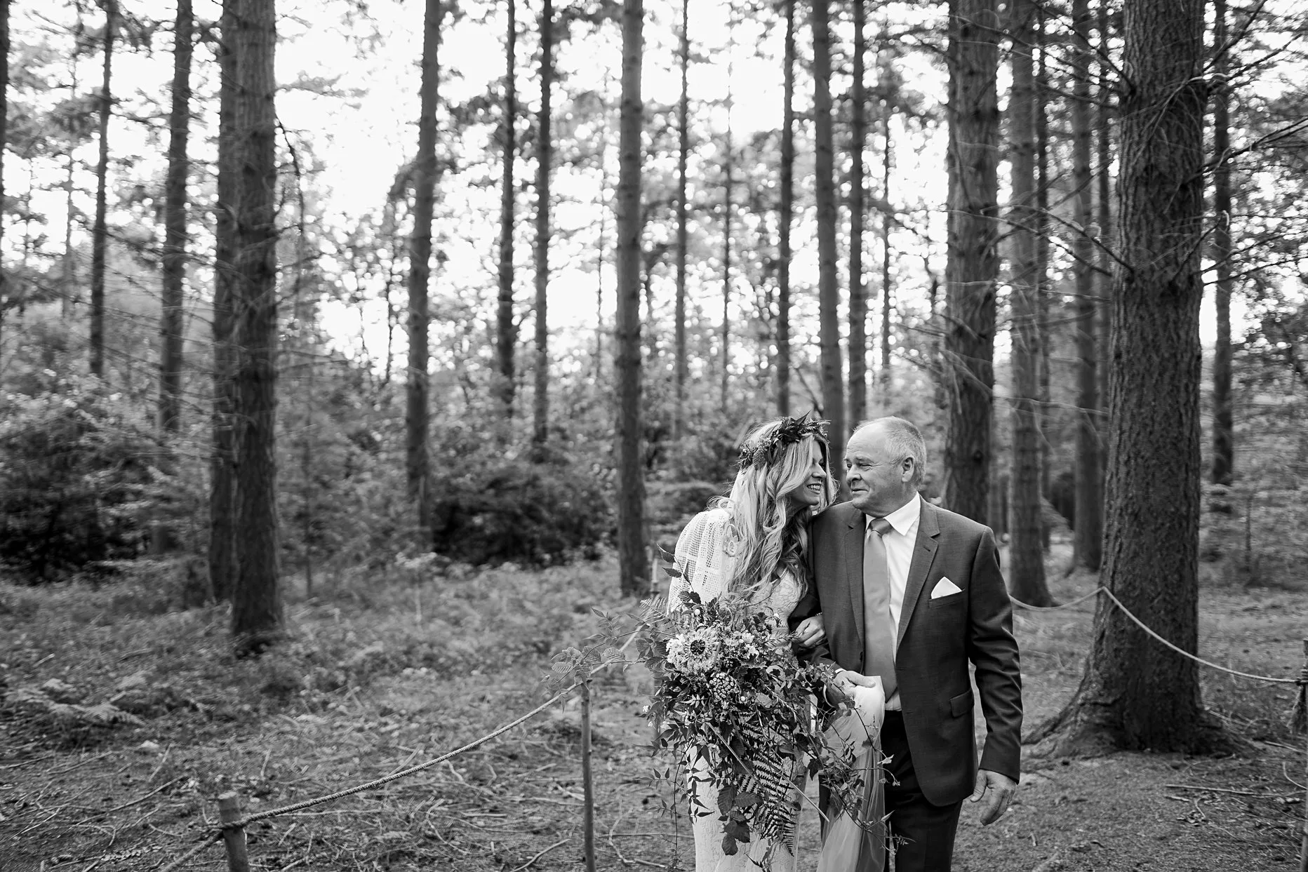 Emotional moment between the bride and her dad. They are walking through the woods to the outdoor ceremony. The brides dad looks emotional, they are looking at each other smiling.