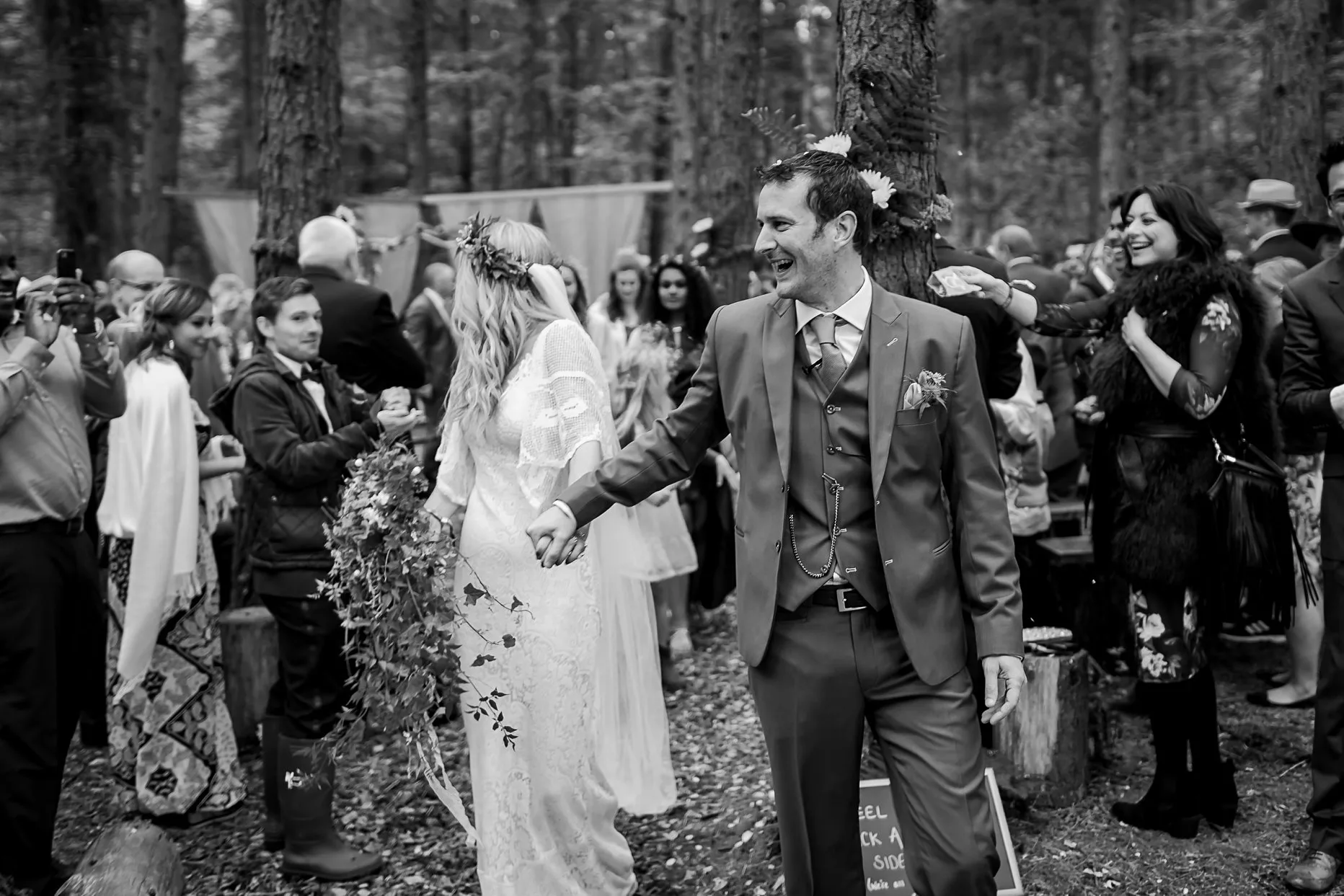 Groom laughing and smiling at wedding guests as he walks with his wife down the aisle.