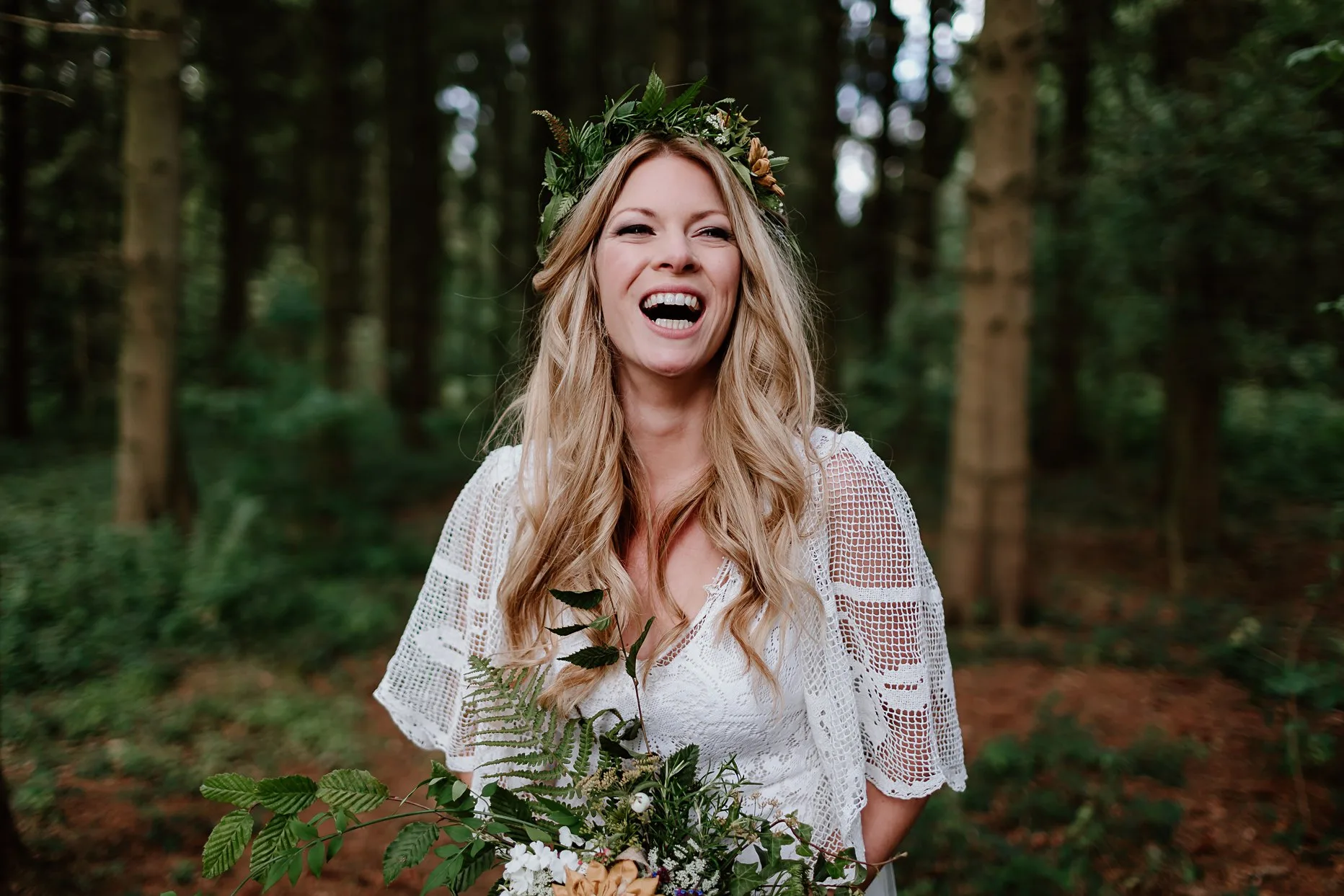 Natural photograph of a bride laughing in the woods at camp katur. She is wearing a foliage flower-crown and a white crochet boho wedding dress.
