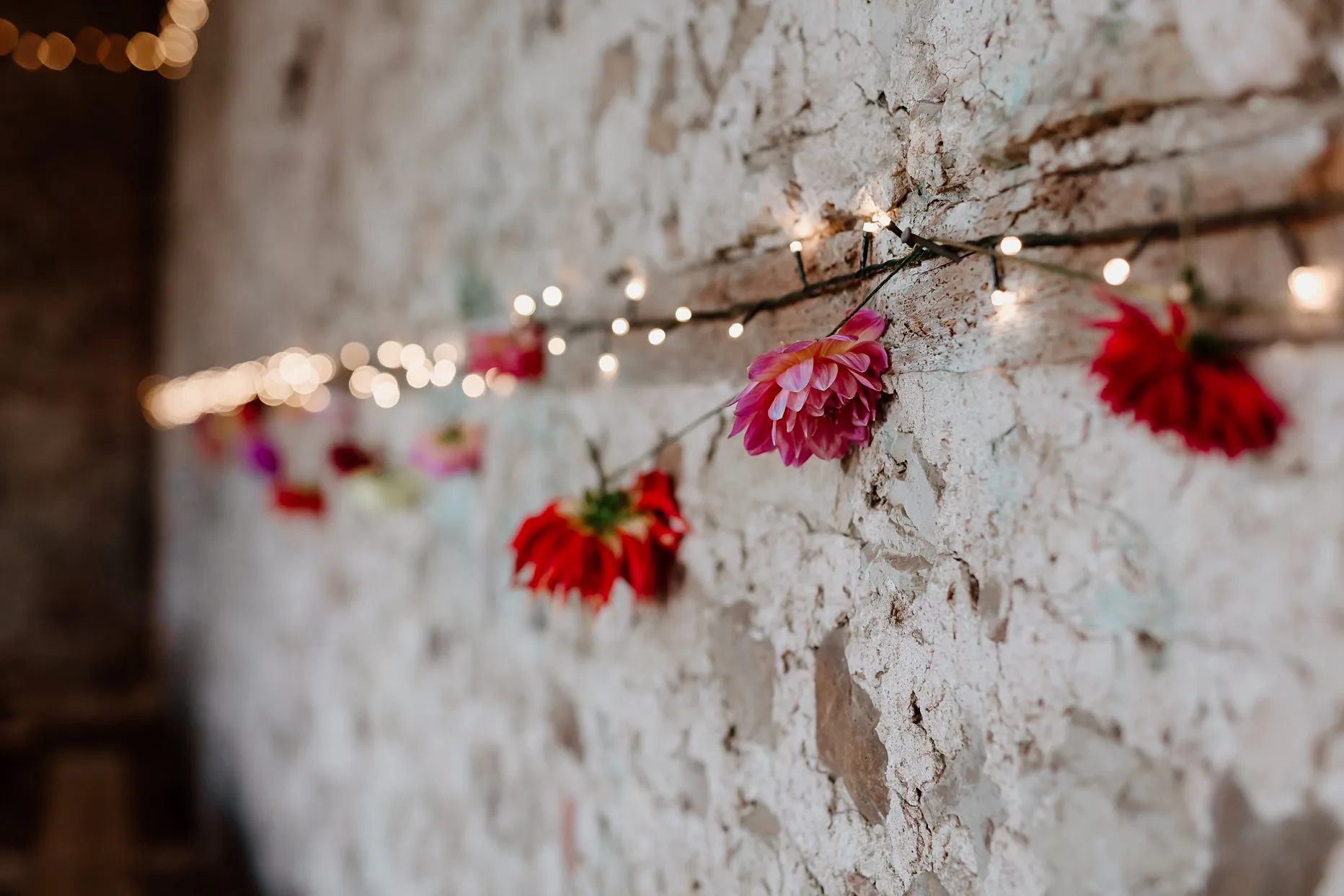 Flowers and fairy lights hanging from a white washed brick wall in the hay barn at Camp Katur.