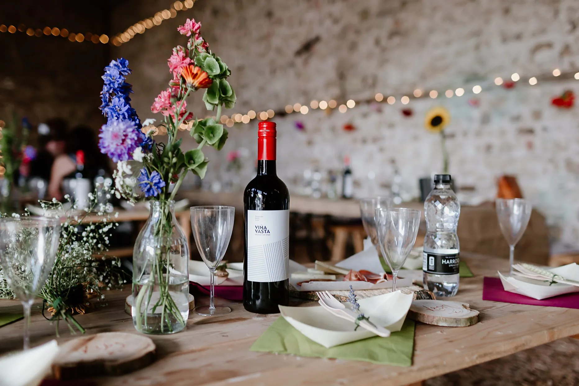 Brightly coloured flowers in a vase next to a bottle of wine. Table dressed for a wedding at Camp Katur.