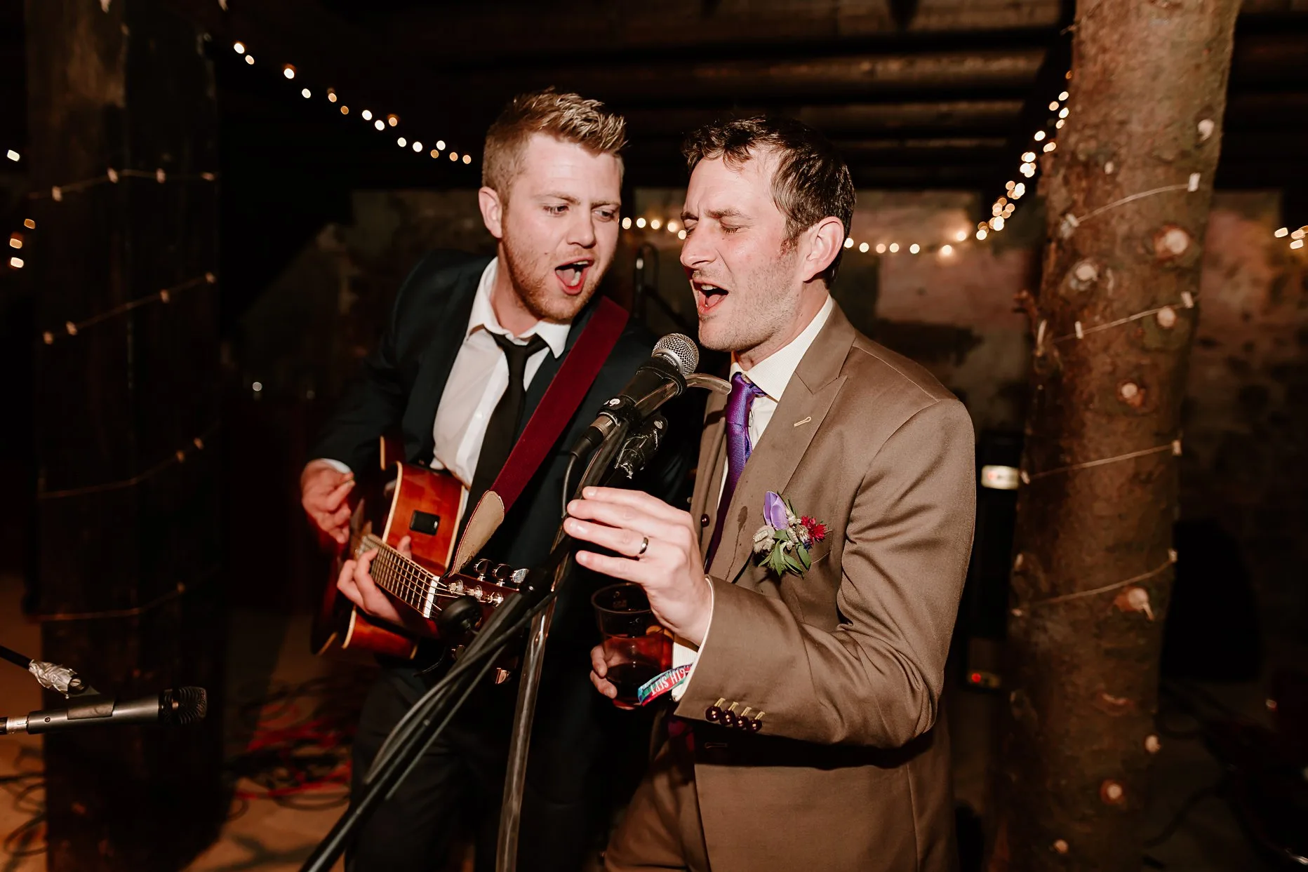 Groom sining into the microphone with another wedding guest holding a guitar.