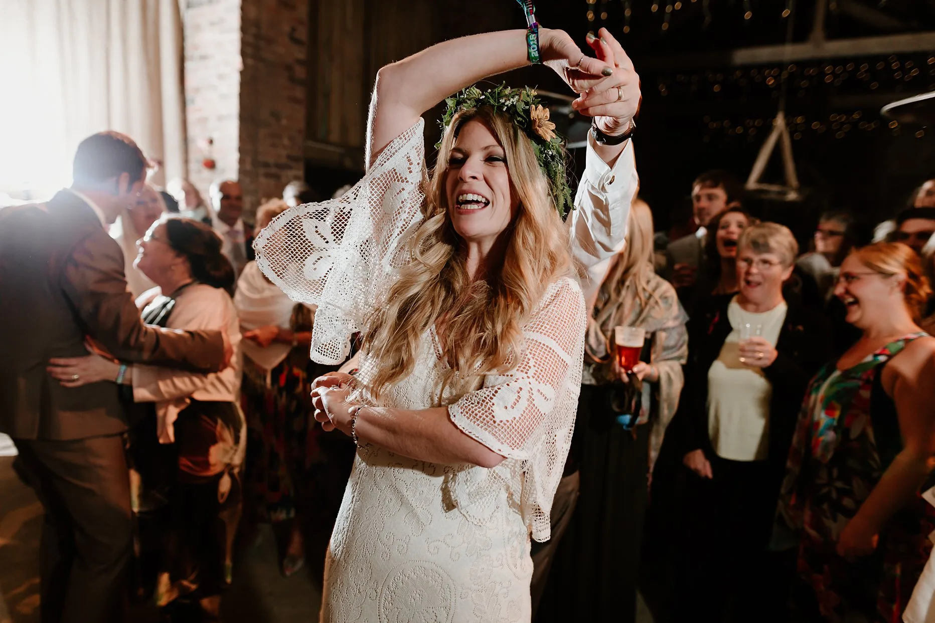 Bride being spun around by a wedding guest. The bride looks happy and is smiling. She is wearing a white crochet wedding dress and foliage flower crown.