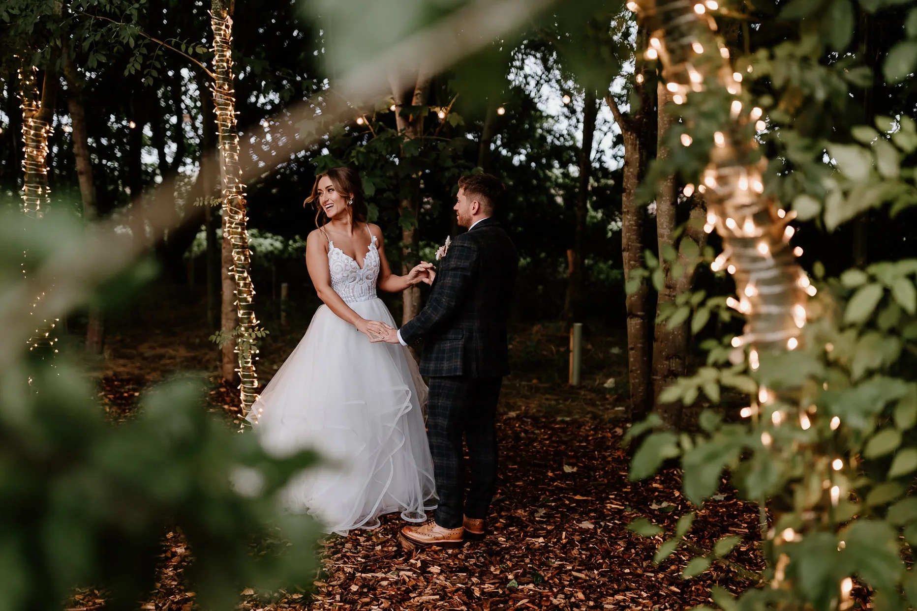 Bride and groom dancing in the woods surrounded by fairylights and trees.