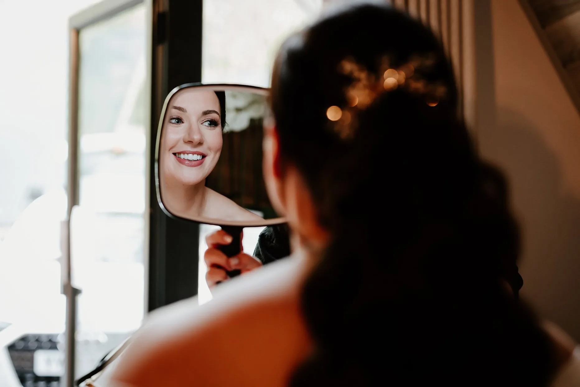 Bride looking in the mirror at her wedding makeup on the morning of her wedding at Oaklands.