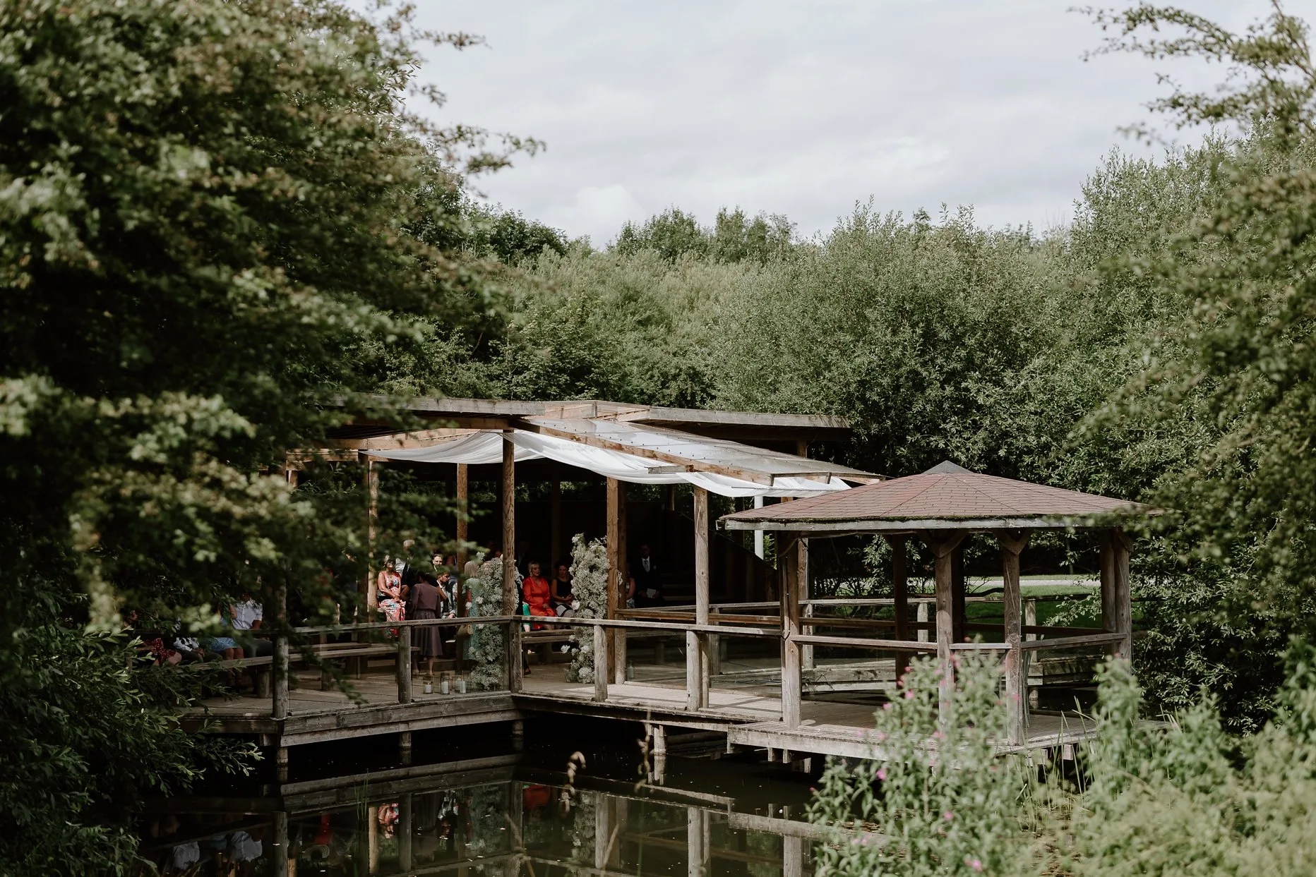 Exterior photograph of the pavilion at Oaklands Driffield. The ceremony area is located over the large lake and surrounded by trees.