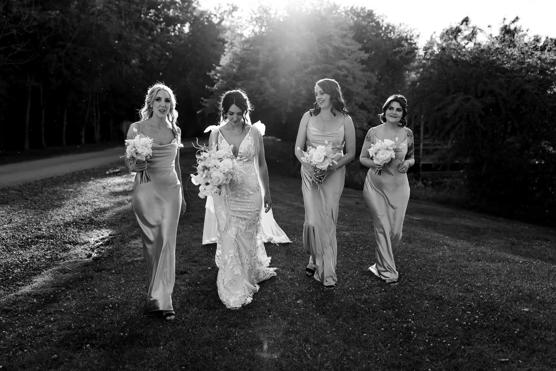 Bride walking with 3 bridesmaids all holding bouquet's. The sun is shining behind them.