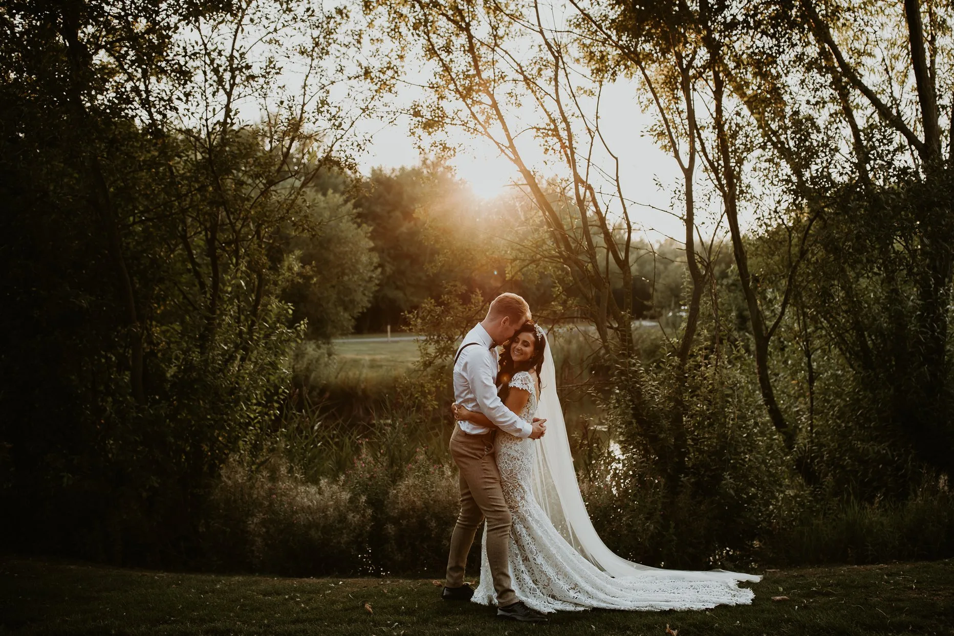 A bride and groom holding each other and smiling. The sun is setting in the background at Oaklands Grand Lodge wedding venue.