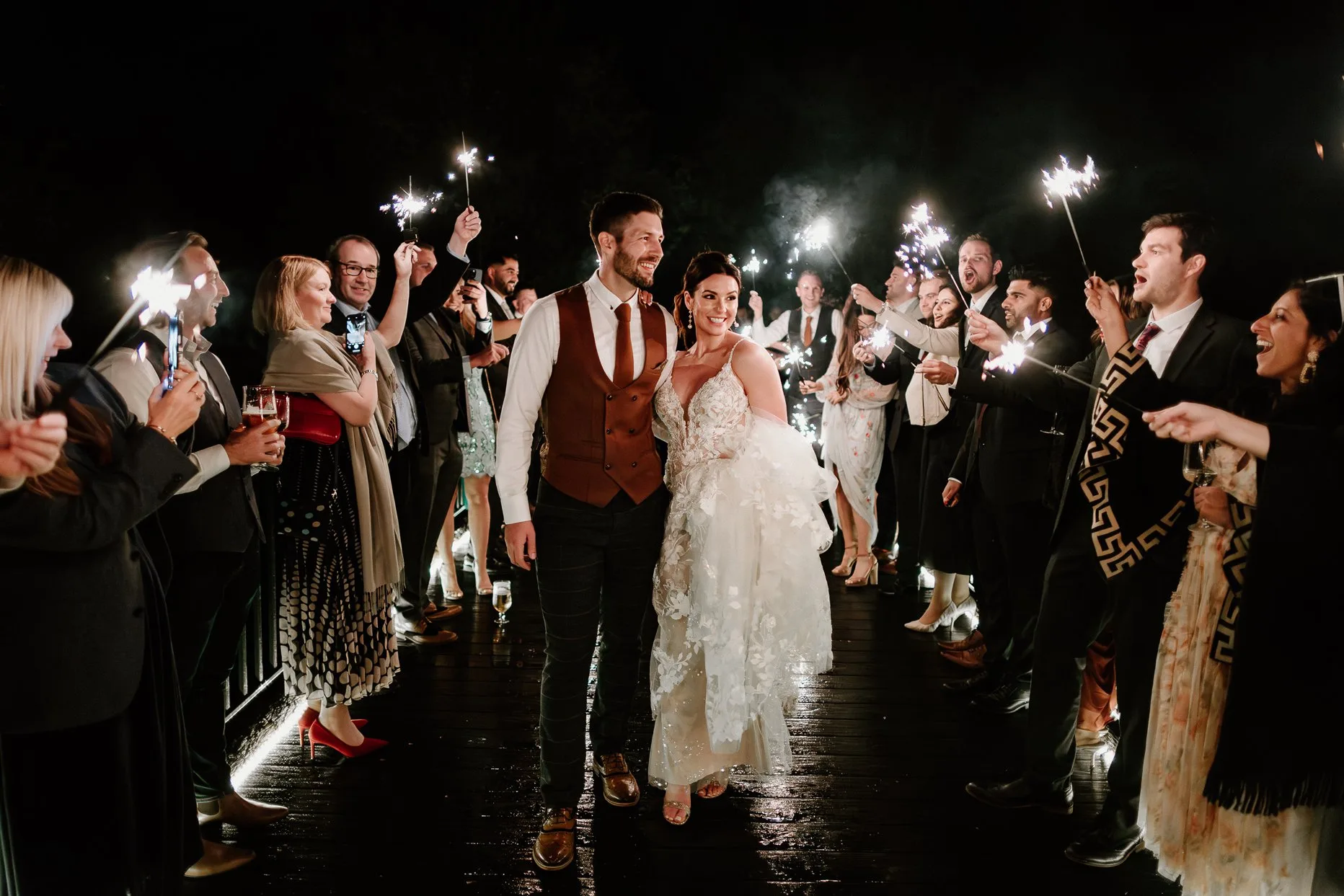 Bride and groom walking through a sparkler tunnel at Oaklands wedding venue in Driffield. Wedding guests stand either side of them holding sparklers in the air.