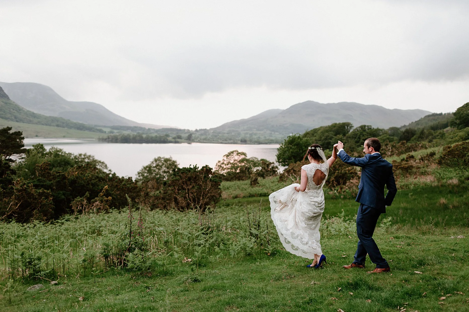 Bride and groom dancing on a hill overlooking Crummock Water in the Lake District. Groom is spinning the bride around.