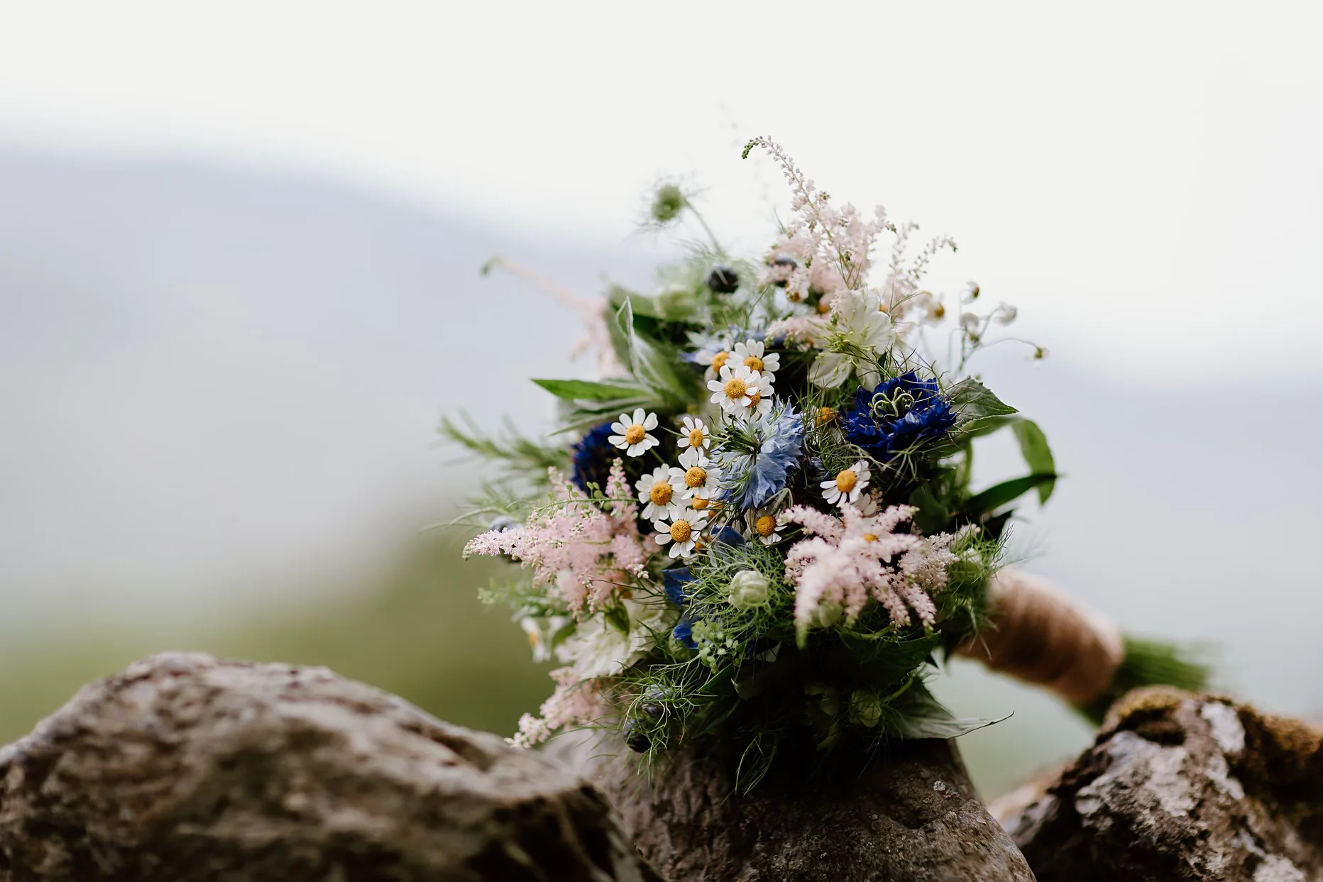 Rustic brides bouquet filled with wild flowers. Rested on a stone wall in the Lake District.