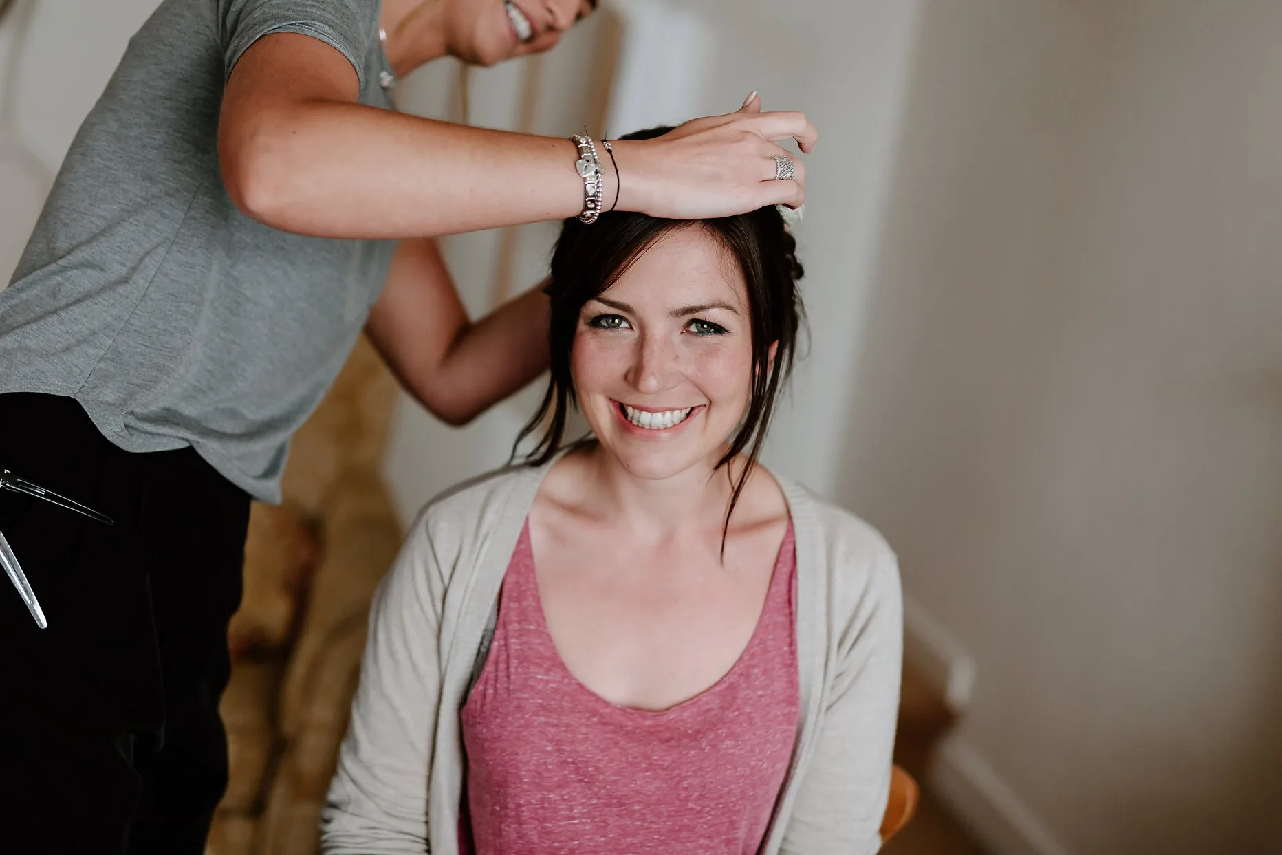 Bride having her hair done on the morning of her wedding. Bride is looking at the camera smiling whilst the hairdresser is placing pins in her hair.