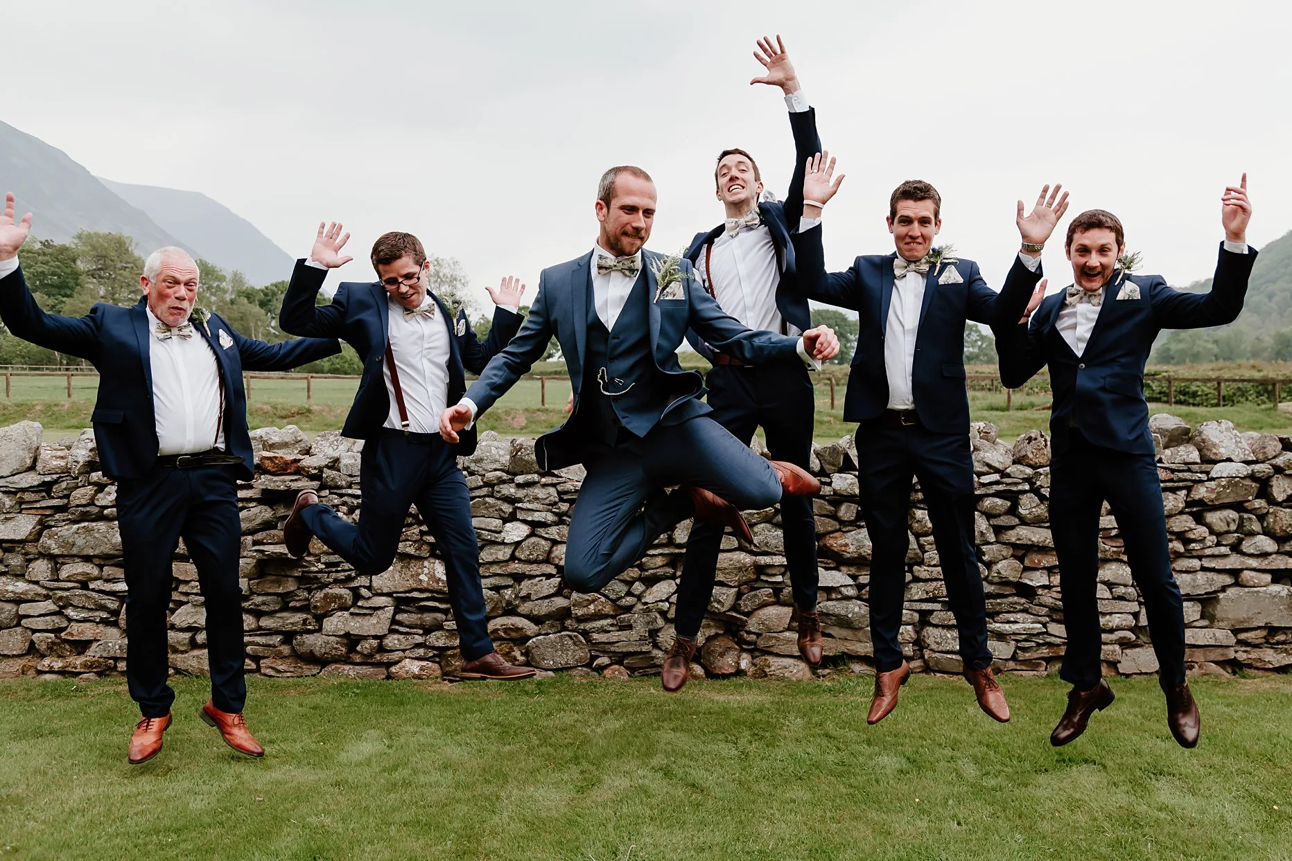 Groom and his groomsmen dressed in blue suits jumping in the air in the gardens of New House Farm wedding barn