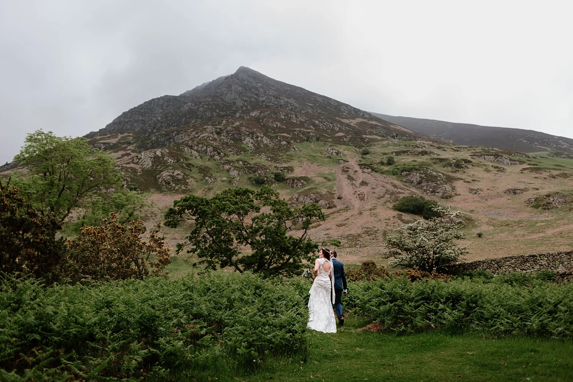 Bride and groom walking through cumbria surrounded by hills and mountains of the Lake District.