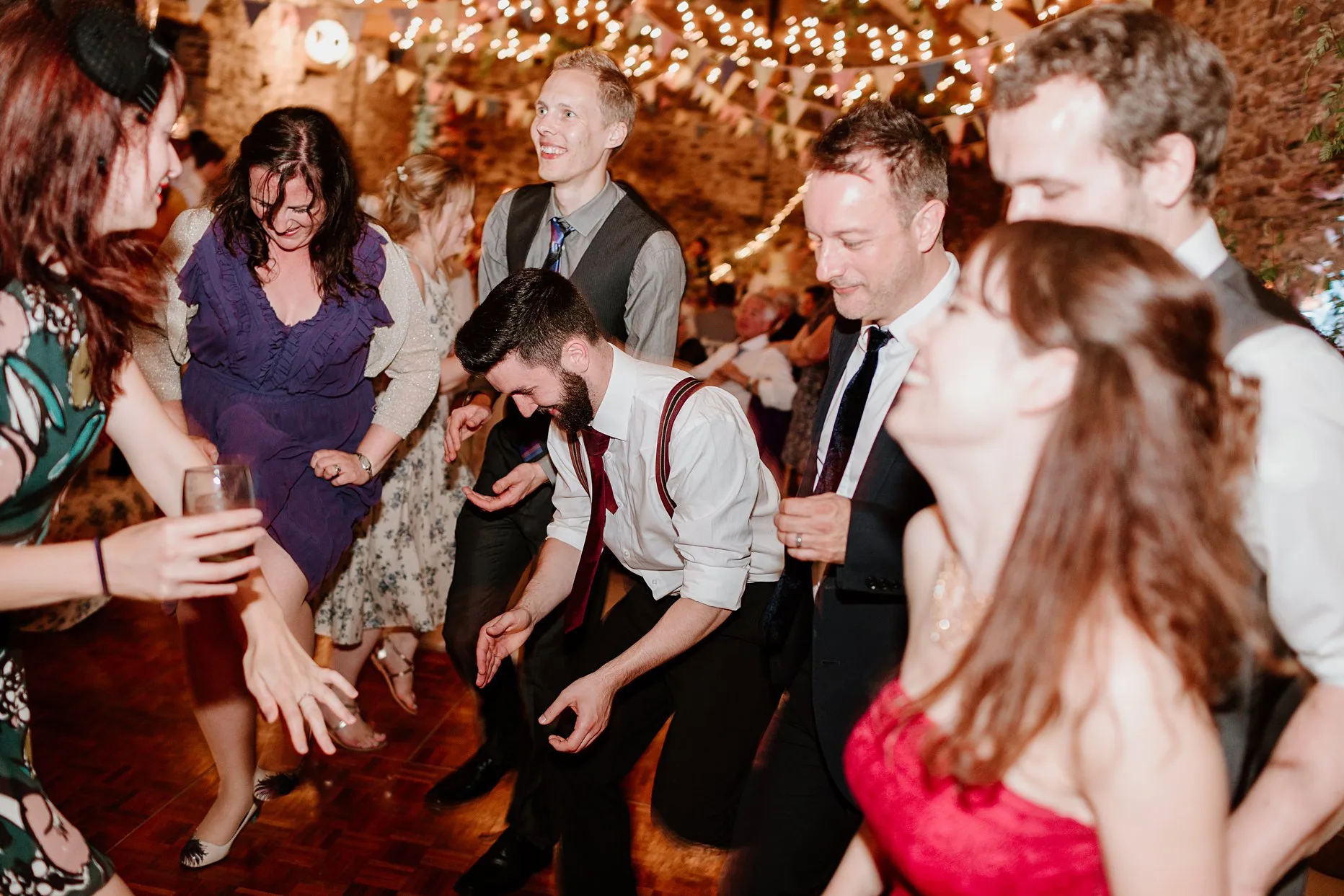 A group of wedding guests dance during the evening reception of their friends wedding. Fairy lights in the background.